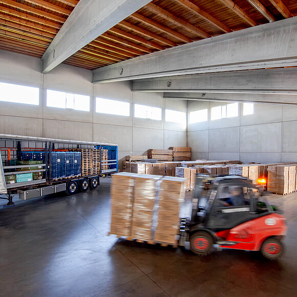 Gabelstapler der Spedition Gelhart fährt Waren in einer Lagerhalle zu einem LKW
